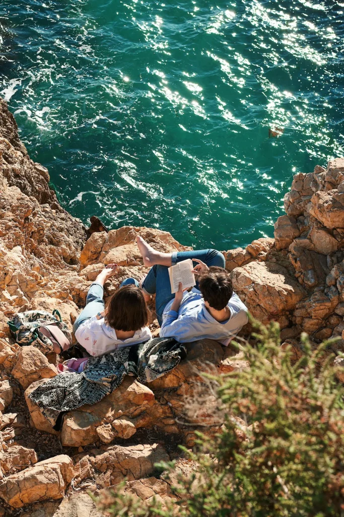People sitting on coastal rocks beside turquoise ocean water in reflective moment